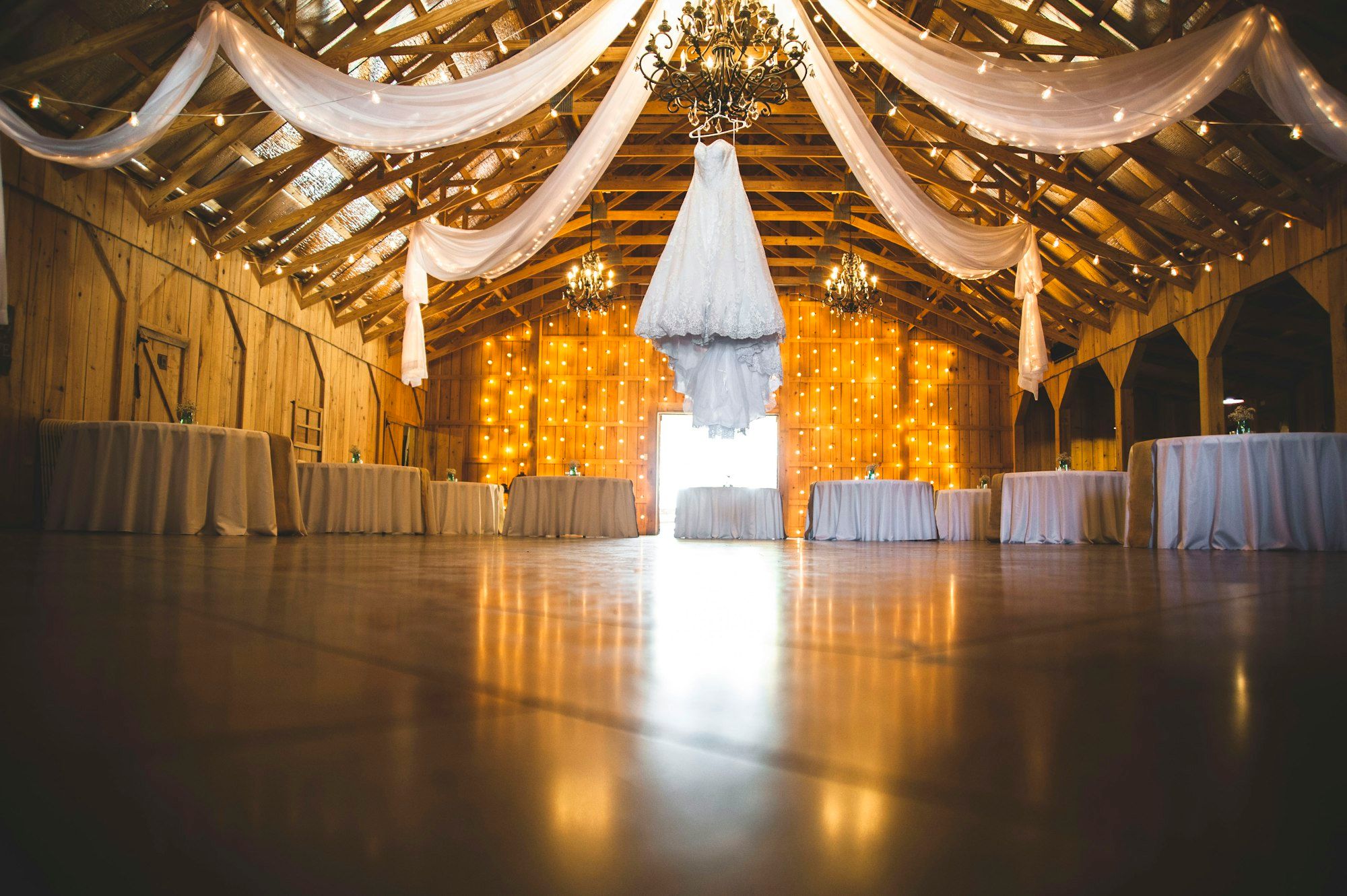 A barn venue with fabric draped from the rafters and a chandelier