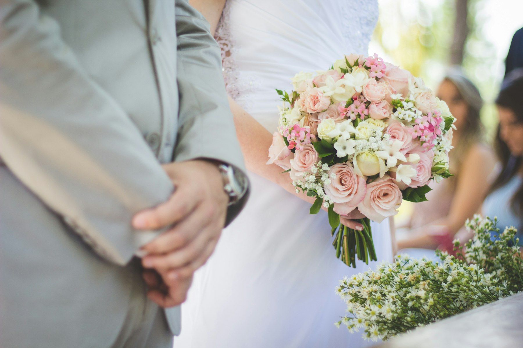 A couple standing close, one holding a bouquet of blush roses and greenery