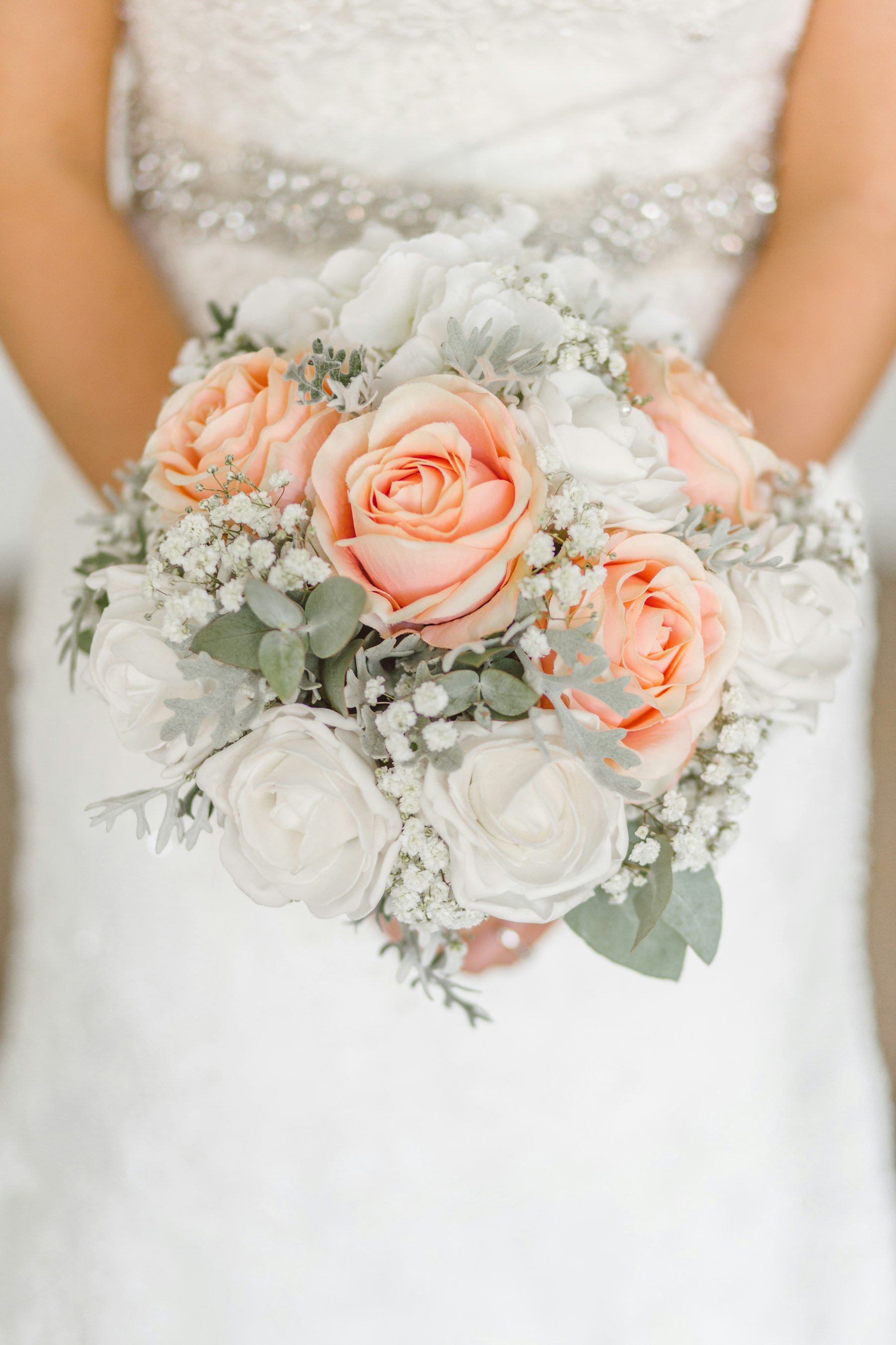 A bridal bouquet of peach and white roses held against a white dress