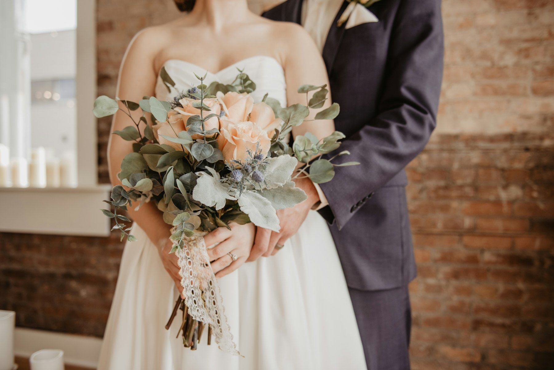 A bride holding a bouquet of peach roses and eucalyptus beside her partner