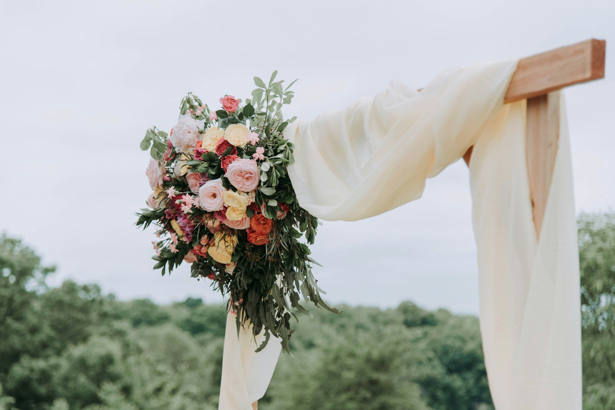A wooden ceremony arch draped with ivory fabric and a cascade of pink and white flowers