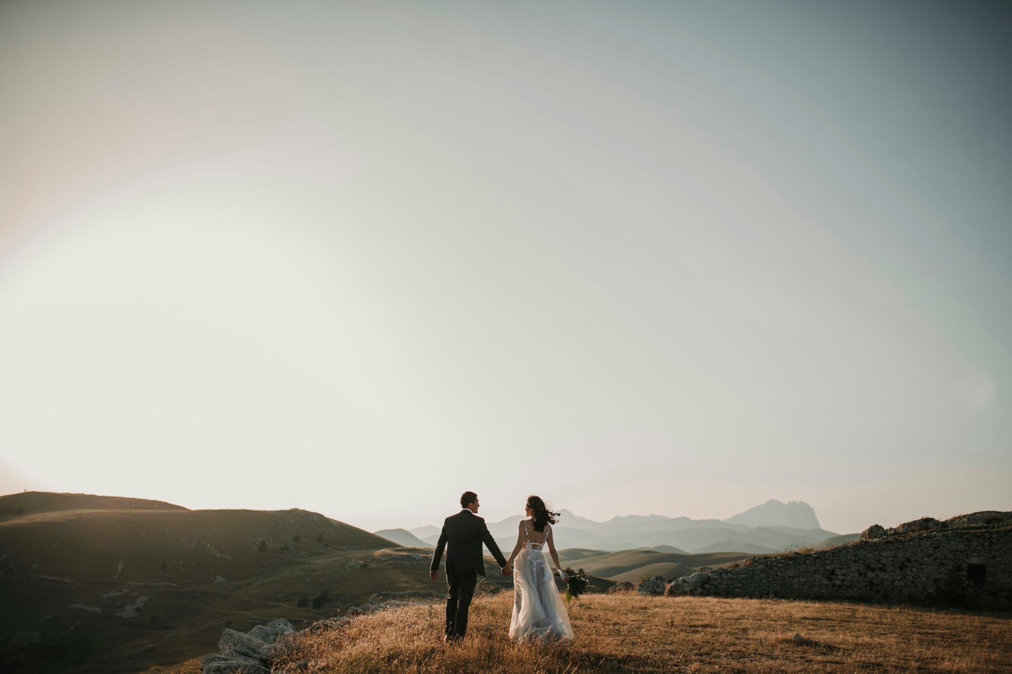 A couple walking hand in hand across open hills toward the mountains