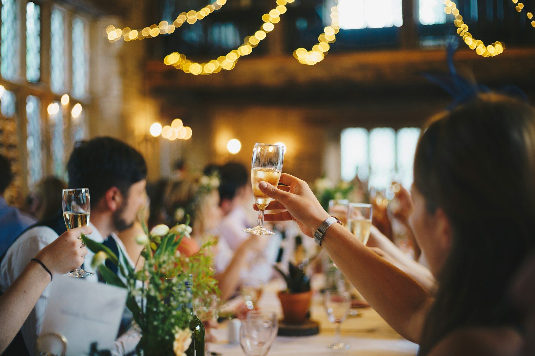 Guests raising glasses in a toast under strings of warm lights