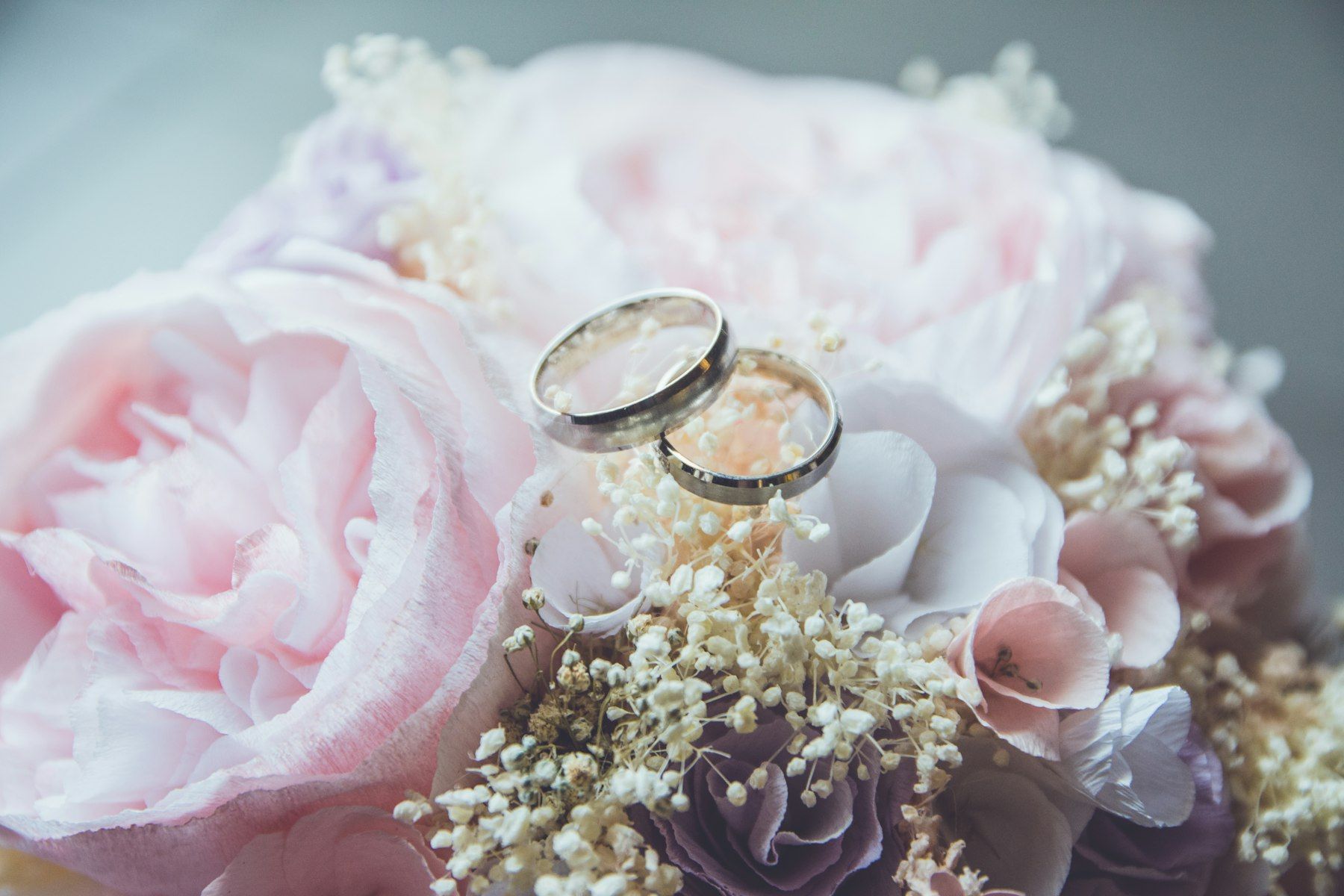 Two wedding rings resting on pink peonies and baby’s breath